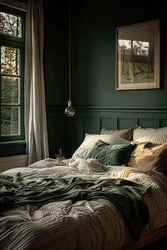 an unmade bed in a dark room with green walls and two framed pictures on the wall