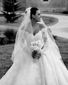 a woman in a wedding dress and veil is standing on the grass with her bouquet