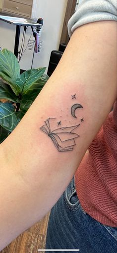 a woman's arm with a book and stars tattoo on the left side of her arm