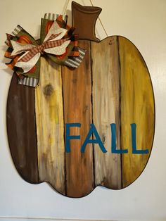 a wooden sign with the word fall hanging on it's side and a bow