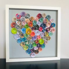 a heart made out of rolled up paper on top of a black table next to a white frame