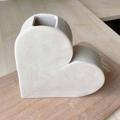 a white heart shaped vase sitting on top of a wooden table