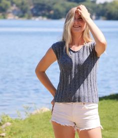 a woman standing in front of a lake with her hands on her head and looking at the camera