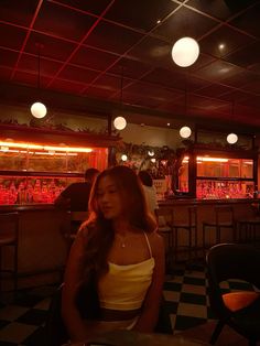 a woman sitting at a table in front of a bar with red lights on the ceiling