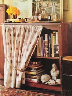 a bookshelf filled with lots of books next to a window covered in curtains