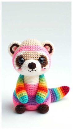 a crocheted raccoon sitting in front of a white background wearing a colorful sweater