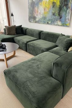 a large green couch sitting in a living room next to a painting on the wall