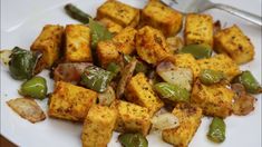 a white plate topped with tofu and green peppers next to a fork on top of a table