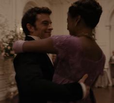 a man in a tuxedo and woman in a purple dress dance together at an event