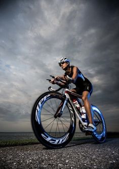 a woman riding a bike on top of a gravel road next to the ocean under a cloudy sky