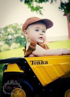 a young boy in a hat is sitting on a toy truck with the word tonka written on it