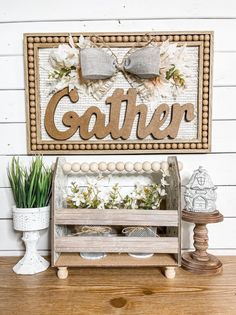 a wooden sign that says gather with flowers in front of it and a potted plant next to it