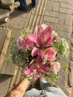 a person holding a bouquet of flowers in their hand while standing on a sidewalk next to a brick walkway