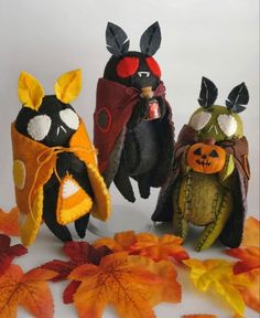 three stuffed animals dressed in halloween costumes with leaves on the ground and one is holding a pumpkin