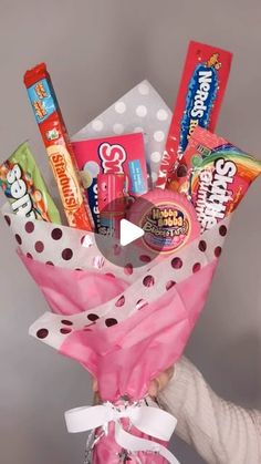 a person holding up a pink bouquet with candy and candies in it's wrap