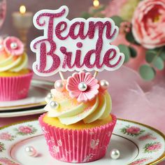 two cupcakes with pink frosting and white icing are on a plate that says team bride