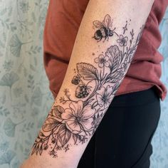 a woman's arm with flowers and bees tattooed on the back of her arm