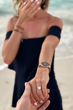 a man and woman holding hands on the beach while looking at each other's fingers