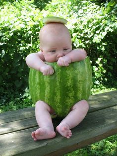 a baby sitting on top of a wooden bench next to a green watermelon