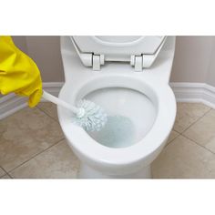 a white toilet with a yellow duster on the lid and a cleaning brush in it