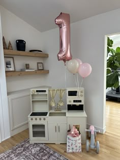 balloons are floating in the air above a toy kitchen and play room set up for a baby's first birthday