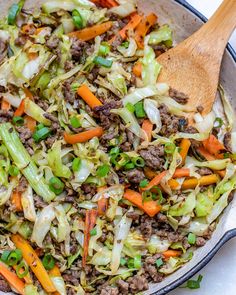 a skillet filled with ground beef, cabbage and carrots next to a wooden spoon