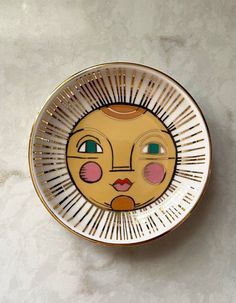 a yellow and white plate with a face painted on the side, sitting on a marble surface