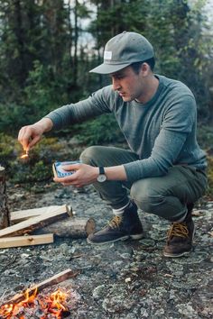 a man sitting on the ground next to a campfire holding a cell phone in his hand