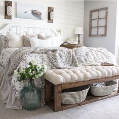 a bed with white sheets and pillows in a bedroom next to a table with baskets on it