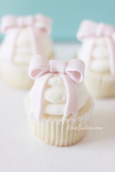 three cupcakes with pink bows and white frosting on top are sitting on a table