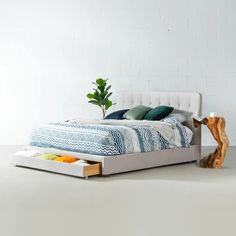 a white bed with blue and green pillows on it's headboard next to a wooden trunk