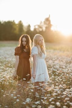 two young women standing in a field of daisies at sunset, with the sun shining on them