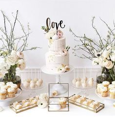 a table topped with cupcakes and cakes next to vases filled with flowers