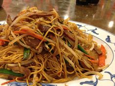 a plate full of noodles and meat with carrots, onions and green peppers on it