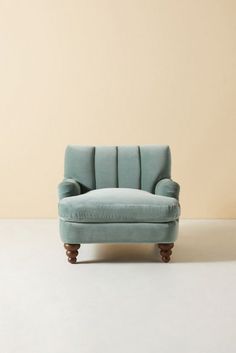 a blue chair sitting on top of a white floor next to a beige wall and wooden legs