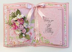 an open birthday card with flowers and ribbons on the front, in pastel pink