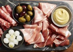 an assortment of meats and olives on a platter with dipping sauce in bowls