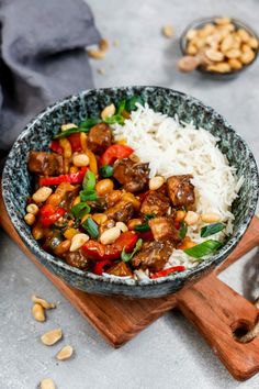 a bowl filled with rice and meat on top of a cutting board next to nuts