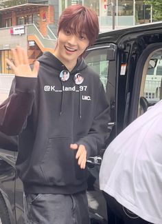 a young man standing in front of a car giving the peace sign