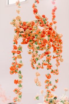 an arrangement of orange and white flowers hanging from the ceiling in front of a window