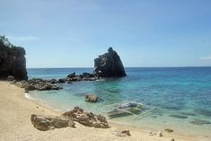 a boat is sitting on the beach next to some rocks and clear blue ocean water