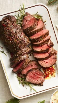 roast beef with herbs and spices on a white plate next to a small bowl of sauce