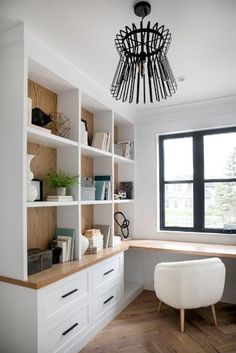 an office with white bookcases and wooden flooring next to a large window