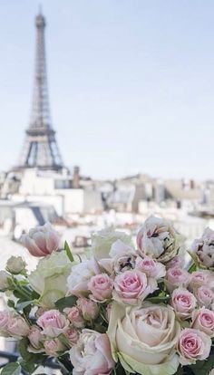 a vase filled with pink and white flowers on top of a metal railing next to the eiffel tower