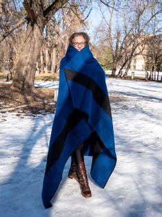 a woman standing in the snow wearing a blue and black blanket