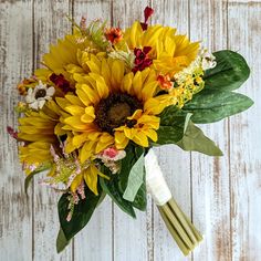 a bouquet of sunflowers and other flowers on a white wooden background with green leaves