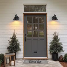 a gray front door with two potted trees on either side and a lantern in the middle