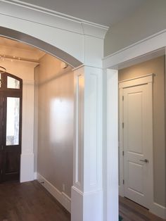 an empty hallway with wooden floors and white walls, leading to a large doorway that leads into another room