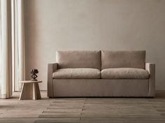 a couch sitting in front of a window next to a small table with a vase on it