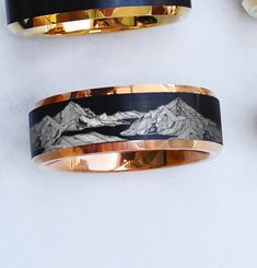 two gold and black bands with mountains on them